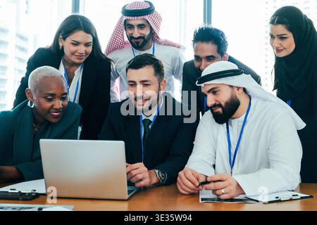 Verschiedene Gruppen von Geschäftsleuten mit unterschiedlichem Hintergrund, die sich um einen Laptop herum versammeln, gemeinsam arbeiten und Strategien in einem modernen Korpo diskutieren Stockfoto