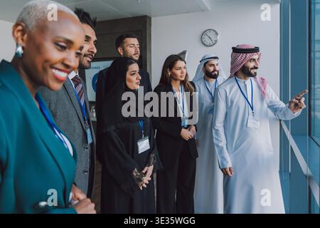 Ein multiethnisches Unternehmensteam hält ein internationales Treffen in einem modernen Bürogebäude in dubai ab, wobei ein Mann beim Gespräch aus dem Fenster zeigt Stockfoto
