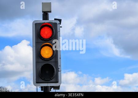 Nahaufnahme einer Ampel mit roten und gelben Signalen vor blauem Himmel, die auf britischen Straßen zum Anhalten vorbereiten. Stockfoto