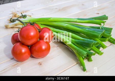 Frische Frühlingszwiebeln und reife Tomaten auf einem Holztisch, bereit zum Zerkleinern und für die Zubereitung der Mahlzeiten in der Küche. Stockfoto