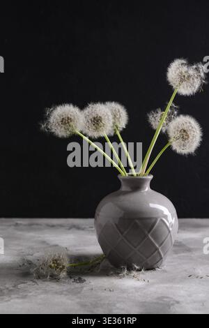 Vase mit wunderschönen Löwenzahnblumen auf dem Tisch vor dunklem Hintergrund Stockfoto