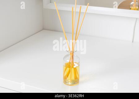 Dieses minimalistische Bild zeigt einen Glasrohr-Diffusor auf einer schlanken weißen Oberfläche. Die Flasche enthält ein lebhaftes gelbes Duftöl und Severa Stockfoto