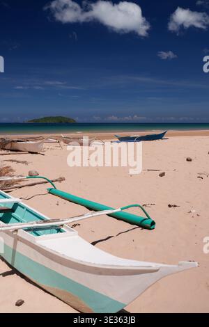 Traditionelle Auslegerboote am Sandstrand mit klarem blauem Himmel und ruhigem Meer. Stockfoto