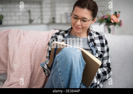 Mädchen in Brille schreibt Notizen in Einem Notizbuch erstellt Eine Liste wichtiger Dinge, die zu Hause zu tun sind Stockfoto