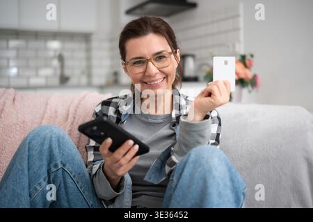 Lächelnde Junge Frau Beim Online-Shopping Mit Smartphone Und Beim Blick In Die Kamera Stockfoto