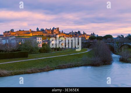 Blick auf den Sonnenuntergang der beleuchteten Cité de Carcassonne in Südfrankreich. Warme Abendfarben erfüllen den Himmel, während die mittelalterliche Festung allmählich erleuchtet Stockfoto