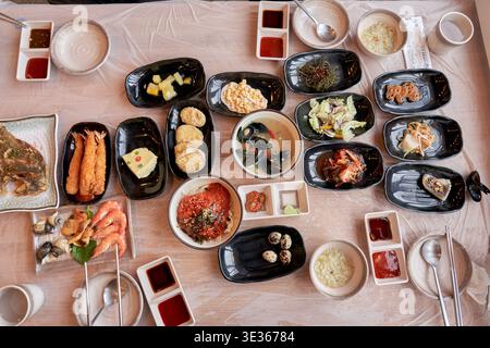 Ein lebhafter Blick über dem Kopf auf ein traditionelles koreanisches Meeresfrüchtegericht mit verschiedenen Banchan, gebratenen Garnelen, Muscheln und rohem Fisch am SOL Beach in Samcheok Stockfoto