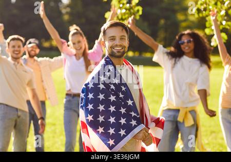 Feiertagsland-Stolz-Party, Mann in die amerikanische Flagge gewickelt, Freunde versammelten sich glücklich Stockfoto
