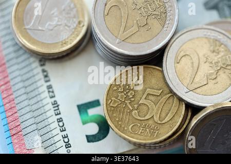 Euro-Geldscheine und Cent-Münzen der Eurozone stapeln sich auf dem Tisch. Münzen der Eurozone auf Euro-Banknoten Nahaufnahme. Das Konzept von Wirtschaft, Steuern und Bankwesen in der Eurozone Stockfoto