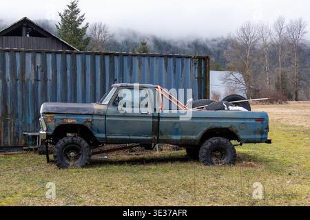 Rostiger blauer Pick-up-Truck, geparkt bei einem Versandcontainer mit nebeligen Bergen in Pemberton, British Columbia, Kanada Stockfoto