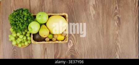 Korb mit frischem Obst und Gemüse auf einer hölzernen Oberfläche mit glattem Hintergrund. Züchten Sie frisches Obst und Gemüse in Korb. Stockfoto