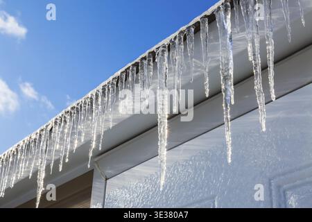 Nahaufnahme langer Eiszapfen, die nach eiskaltem Regen im Spätwinter vom Dach der Asphaltschindeln auf dem Lagerschuppen hängen, Quebec, Kanada Stockfoto
