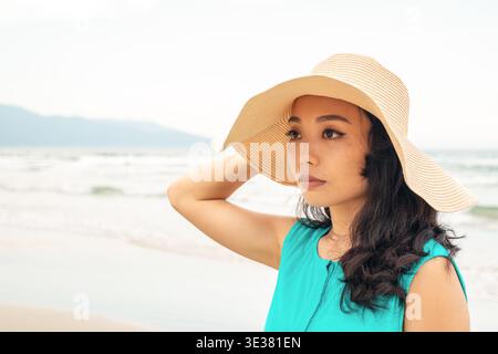 Junge asiatische Frau mit Strohhut genießt einen ruhigen Sommerurlaub an einem wunderschönen Strand. Für Reise-Blogs, Urlaubsangebote und Lifestyle-Inhalte. Stockfoto