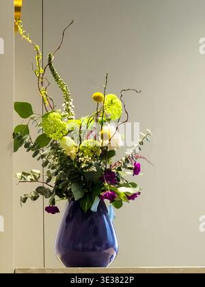 Atemberaubendes modernes Blumenarrangement in glänzender kobaltblauer Vase mit gemischtem Grün und leuchtenden Blüten Stockfoto
