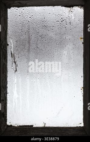 Wassertropfen aus schmelzendem Schnee auf der Oberfläche des beschlagenen Fensters in einem alten Landhaus im Winter Stockfoto
