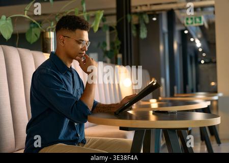 Seitenansicht eines fokussierten jungen Geschäftsmannes, der ein digitales Tablet verwendet, während er nachts allein in der Bürolounge sitzt Stockfoto