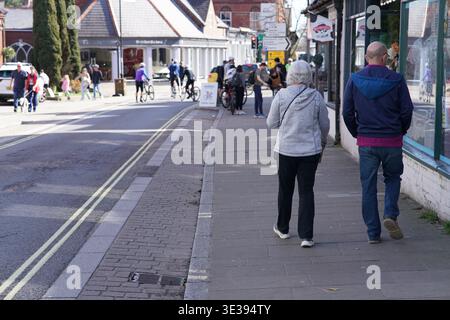 Älteres Ehepaar spazieren entlang der sonnigen Hauptstraße in Lyndhurst, New Forest, Hampshire, England. Lyndhurst, England Stockfoto