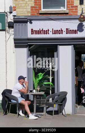 Mann, der einen Drink an einem Tisch im Freien vor dem Café „The Forager“ in Lyndhurst, New Forest, Hampshire, England genießt. Lyndhurst, England Stockfoto