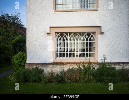 Weiß verputztes Gebäude mit unverwechselbaren gotischen Fenstern mit Bogengewölbe, wahrscheinlich Teil eines historischen Anwesens mit Garten. Stockfoto