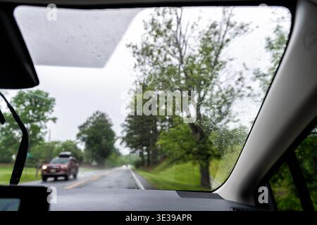 Abstrakter pov-Passagierperspektive von nassen Regenfällen auf Windschutzscheibe und Scheibenwischern bei modernen Fahrzeugen mit gps-Bildschirm im ländlichen Sommerstraßenverkehr Stockfoto