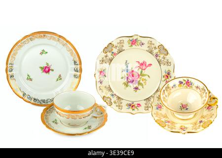 Ein raffiniertes Set aus antikem Geschirr zeigt zarte Blumenmuster und opulente goldene Ränder in einer klaren Komposition. Stockfoto