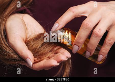 Weibliche Hände tragen Öl oder Serum auf die Haarspitzen auf. Haarpflegeprogramm und Schönheitsbehandlungskonzept. Kosmetisches Produkt für gesundes glänzendes Haar verwendet. Stockfoto