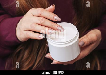 Weibliche Hände, die ein weißes Kosmetikglas halten. Hautpflegeprodukt für die tägliche Schönheitsroutine. Creme-Behälter in einer einfachen und sauberen Nahzusammensetzung dargestellt Stockfoto