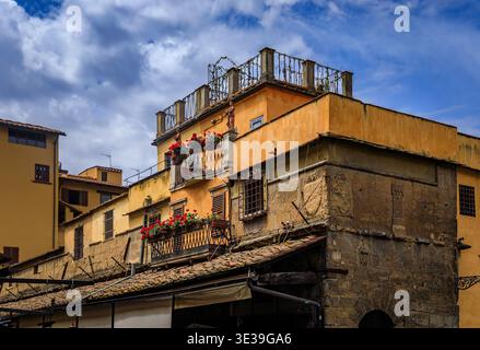 Die mittelalterlichen Steinbauten der Ponte Vecchio in Florenz, Italien, mit verwitterten gelben Fassaden, blumengefüllten Balkonen und rustikalen Ziegeldächern Stockfoto