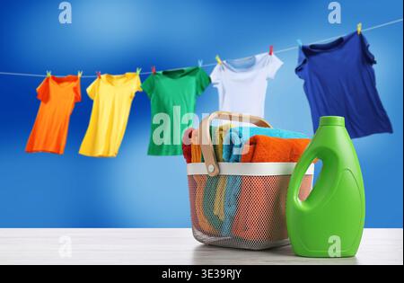 Wäschekorb mit sauberen Handtüchern und einer Flasche Waschmittel auf dem Tisch. Kleidung, die am Himmel trocknet Stockfoto