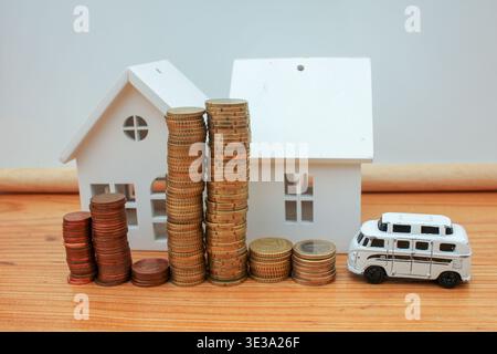 Ein Stapel Euro-Münzen vor winzigen Holzhäusern und einem Spielzeugfahrzeug. Eine visuelle Metapher für die Budgetierung der Familie, die Einsparung für eine Anzahlung auf ein f Stockfoto