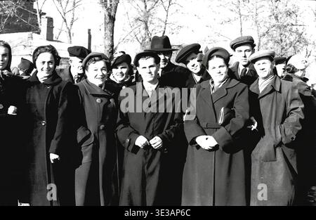 Vintage-Porträt aus den 1950er-1960er-Jahren, das eine große, fröhliche Gruppe von Fabrikangestellten zeigt, die an einem sonnigen Wintertag in Slawjansk gemeinsam posiert. Männer und Frauen tragen schwere Mäntel, Hüte und Tücher und nehmen an einer feierlichen öffentlichen Demonstration oder Gemeindeversammlung teil. Das Bild fängt die authentischen Gesichter, die starken sozialen Bindungen und den widerstandsfähigen kollektiven Geist der sowjetischen ArbeiterInnenklasse vor dem Krieg ein und dokumentiert die lebendigen alltäglichen menschlichen Verbindungen eines historisch friedlichen Donbas. Stockfoto
