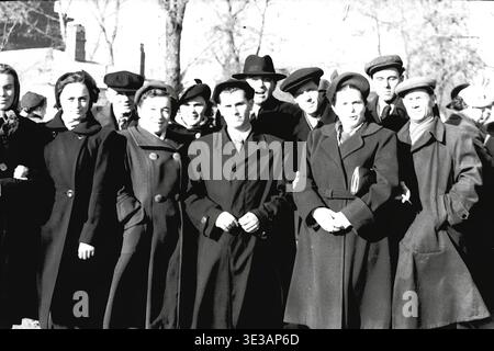 Vintage-Porträt aus den 1950er-1960er-Jahren, das eine große, fröhliche Gruppe von Fabrikangestellten zeigt, die an einem sonnigen Wintertag in Slawjansk gemeinsam posiert. Männer und Frauen tragen schwere Mäntel, Hüte und Tücher und nehmen an einer feierlichen öffentlichen Demonstration oder Gemeindeversammlung teil. Das Bild fängt die authentischen Gesichter, die starken sozialen Bindungen und den widerstandsfähigen kollektiven Geist der sowjetischen ArbeiterInnenklasse vor dem Krieg ein und dokumentiert die lebendigen alltäglichen menschlichen Verbindungen eines historisch friedlichen Donbas. Stockfoto