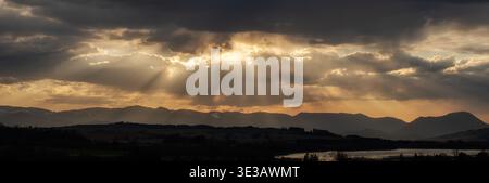 Dramatische Sonnenstrahlen, die durch Wolken über die Berglandschaft in der Region Liptov in der Slowakei brechen. Goldenes Sonnenuntergangslicht, das Silhouetten von Velka Fa beleuchtet Stockfoto