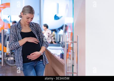 Junge schwangere Frau in ein modernes Büroumfeld. Konzept der Work-Life-Balance, weibliche Empowerment, Karriere in der Schwangerschaft und modernes Busin Stockfoto