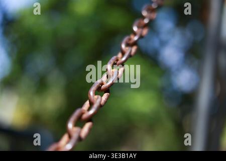 Nahaufnahme einer rostigen Metallkette mit starken Gliedern vor verschwommenem grünem Hintergrund. Alte, schwere Eisenkette, die Konzepte von Verbindung, Sicherheit und en zeigt Stockfoto