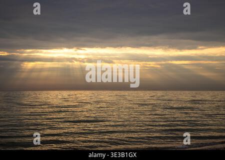 Ozeanbild mit Sonnenstrahlen, die durch die Wolken darüber leuchten und einen dramatischen Naturhintergrund schaffen Stockfoto