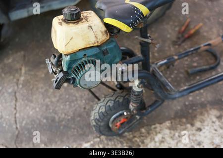 Ein alter, dreckiger Gasroller mit rostigem Motor, der auf Betonboden steht. Ein kaputtes Fahrzeug sieht vernachlässigt und vergessen aus, ein Stück Müll aus der Vergangenheit Stockfoto