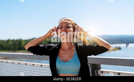 Porträt einer fröhlichen jungen erwachsenen Frau in kabellosen Kopfhörern im Freien. Stockfoto