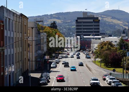 Verkehr entlang einer zentralen Dunedin Straße mit Hügeln im Hintergrund, Otago, Südinsel, Neuseeland. Stockfoto
