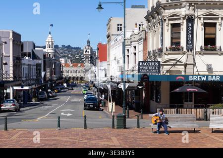 Blick auf die Straße in Richtung Bahnhof Dunedin mit Musiker im Vordergrund, Dunedin, Otago, Südinsel, Neuseeland. Stockfoto
