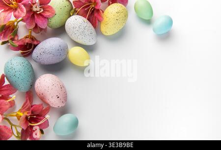 Pastellfarbene gesprenkelte Eier mit roten Blüten bilden eine festliche Weihnachtsgrenze auf weiß Stockfoto