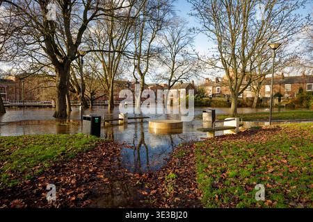 Ein Pfad führt durch einen Stadtpark zu einem überfluteten Gebiet durch einen Fluss mit Häusern im Hintergrund, City of York, England. Stockfoto