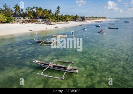 Blick aus der Vogelperspektive auf traditionelle Holzboote, die in klarem türkisfarbenem Wasser an einem tropischen weißen Sandstrand mit Palmen und Resorts ankern. Ort: Zan Stockfoto