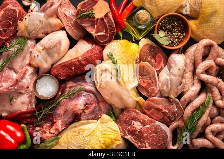 Verschiedene Fleischstücke sind auf dunkler Oberfläche angeordnet. Rindersteaks, Wachteln, Schweinefleischwürste, truthahn, Huhn, und Schweinefleisch sind zusammen mit Kräutern und spi vorhanden Stockfoto