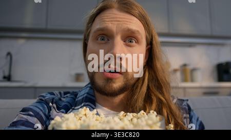 Kaukasischer Mann männlicher Kerl isst Popcorn während er Fernsehserien zu Hause ansieht Wochenende entspannend Fernsehen Filmprogramm Medien Film Snack drinnen genießen Stockfoto