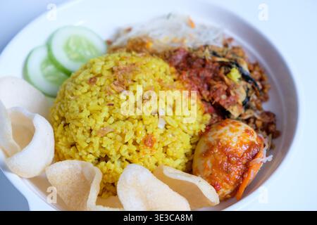 Indonesischer Kurkuma-Reis oder nasi kuning ist aromatischer Reis, der mit Kurkuma und aromatischen Gewürzen zubereitet wird und mit traditionellen Beilagen serviert wird Stockfoto