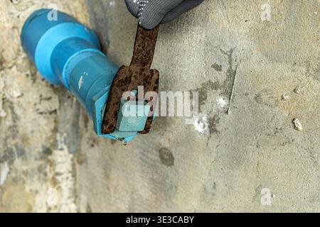 Nahaufnahme eines Arbeiters, der graue Handschuhe trägt, mit einem stark korrodierten, rostigen Flachschlüssel zum Einstellen oder Festziehen eines blauen PVC-Wasserrohrventils, das auf einem liegt Stockfoto