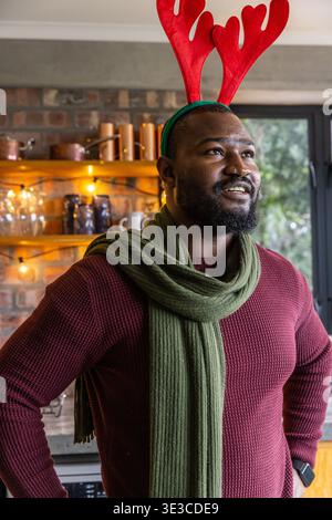 Afroamerikaner Erwachsener stehend, mit rotem Geweih Stirnband, grünem Schal, Pullover in der Küche Stockfoto