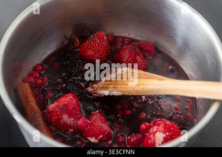 Kochen gemischter Beeren, einschließlich Erdbeeren, Brombeeren und roten Johannisbeeren, in einem metallischen Topf mit einem Holzlöffel und Zimtstab, köcheln lassen Stockfoto