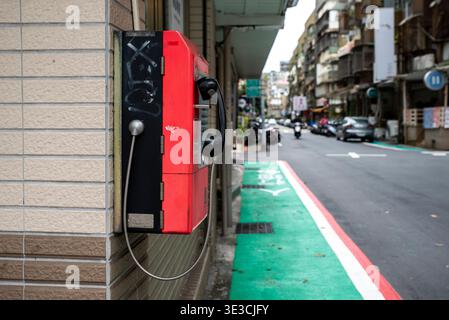 Rote Vintage-Telefonzelle steht an der Straßenecke der Stadt. Der grüne Fahrradweg erstreckt sich entlang einer ruhigen Straße. Gebäude säumen die Straße mit verblassten Schildern. Szene fühlt sich an c Stockfoto